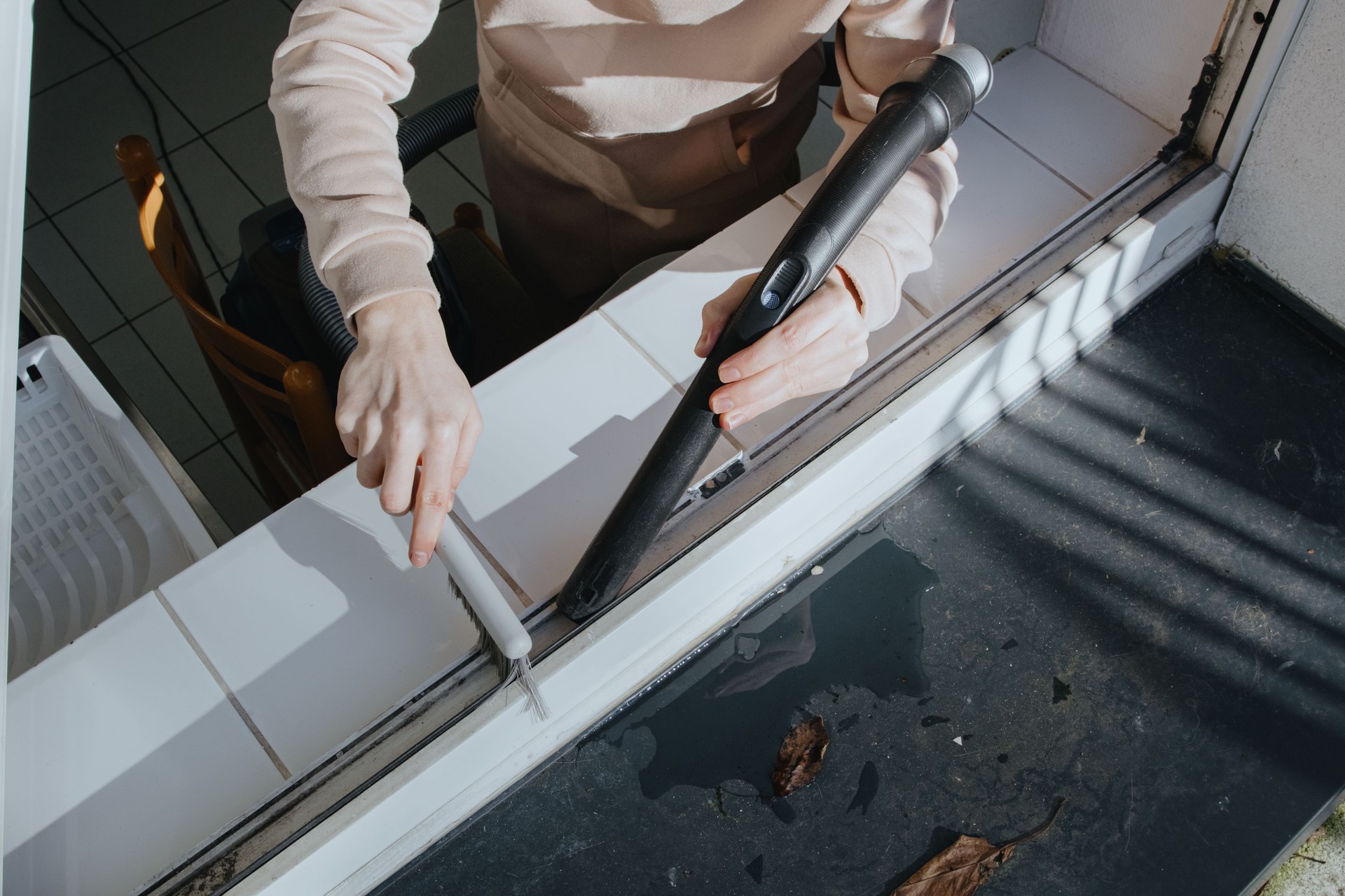 Hands of a man vacuums debris from the window frame. 